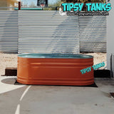 Orange metal tank with 'Tipsy Tanks' branding against a corrugated metal wall.