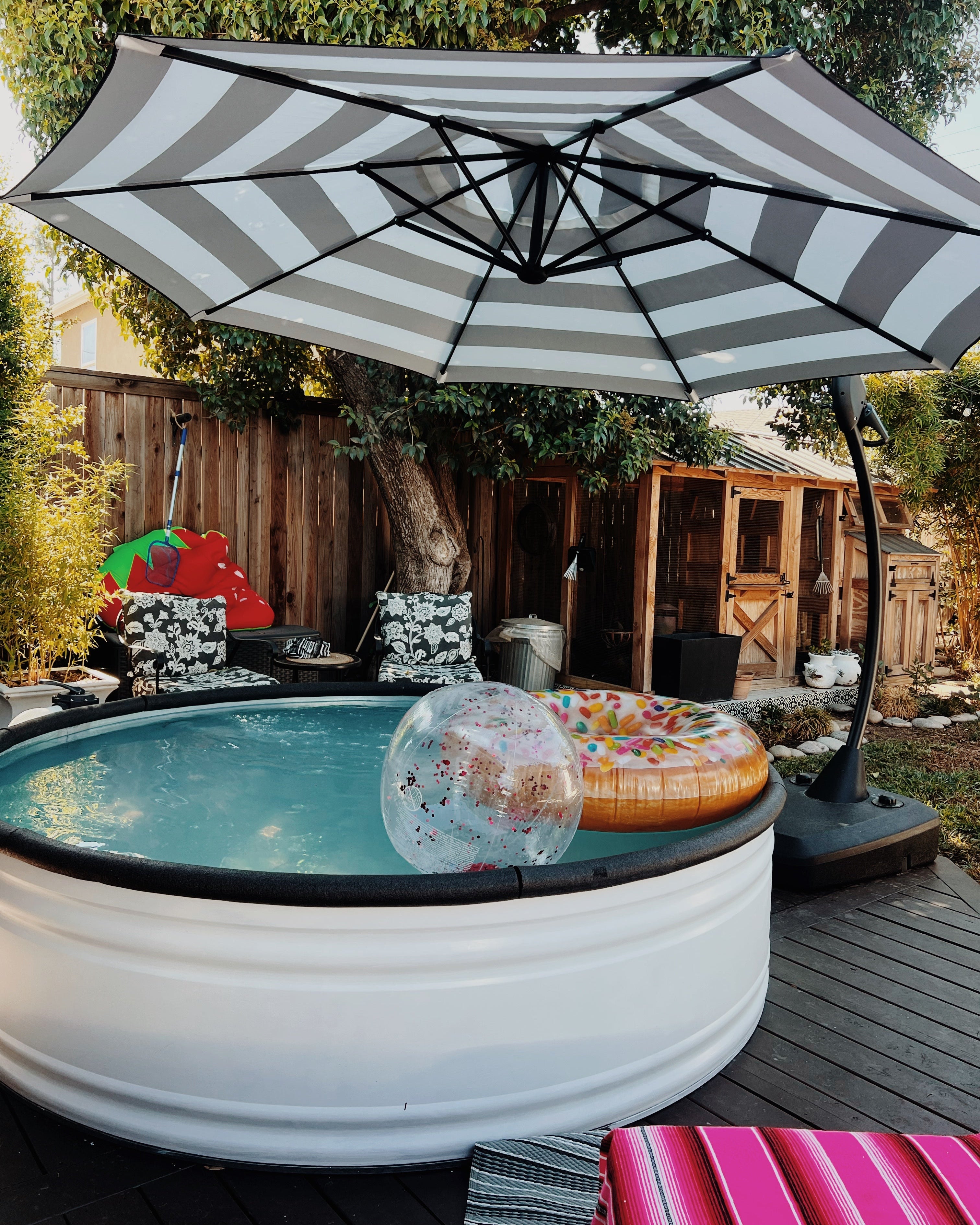 Portable 8ft stock tank pool painted white with striped umbrella on a wooden deck.